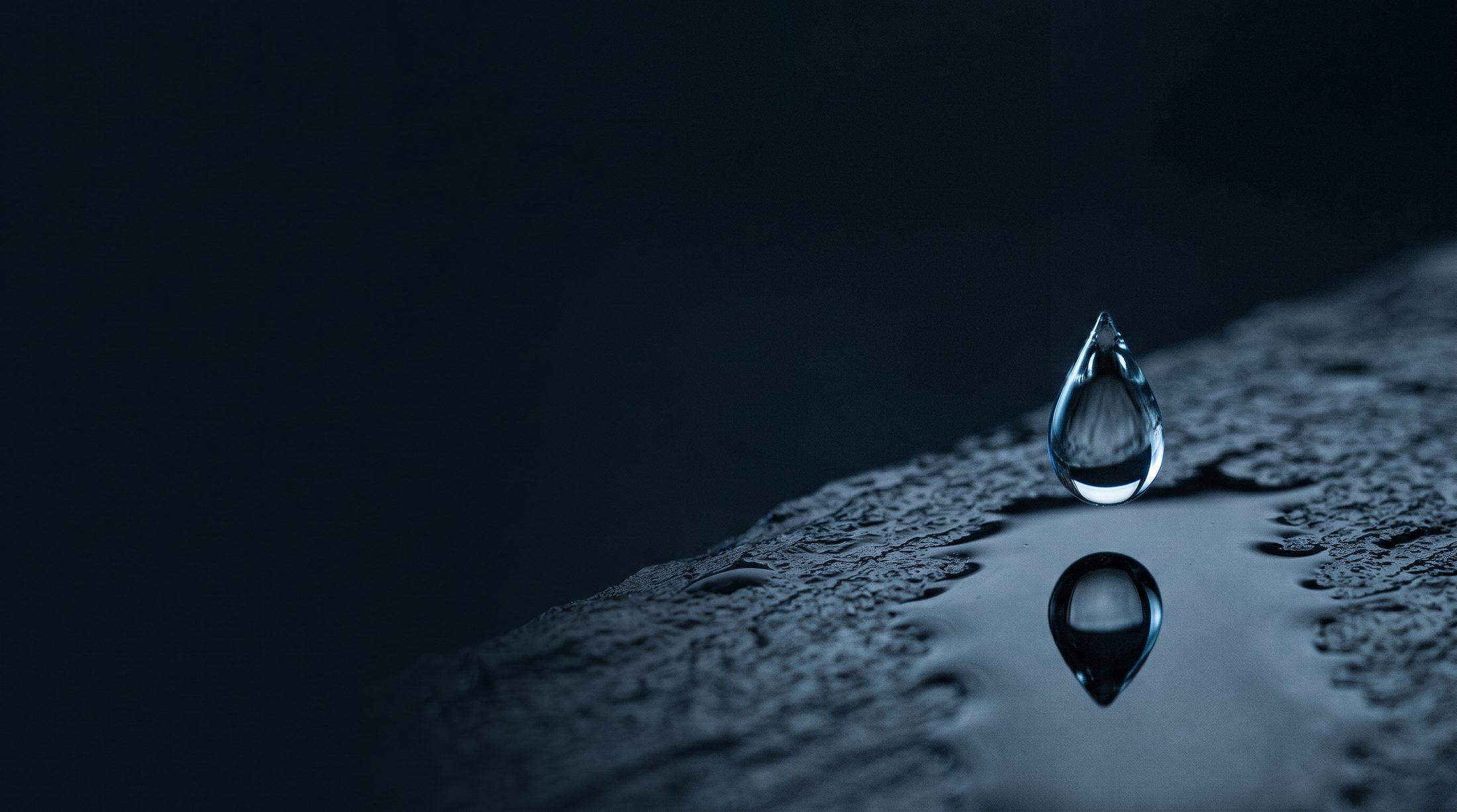 Une goutte d'eau sur une ardoise sombre, image de matière du cabinet LAWBE